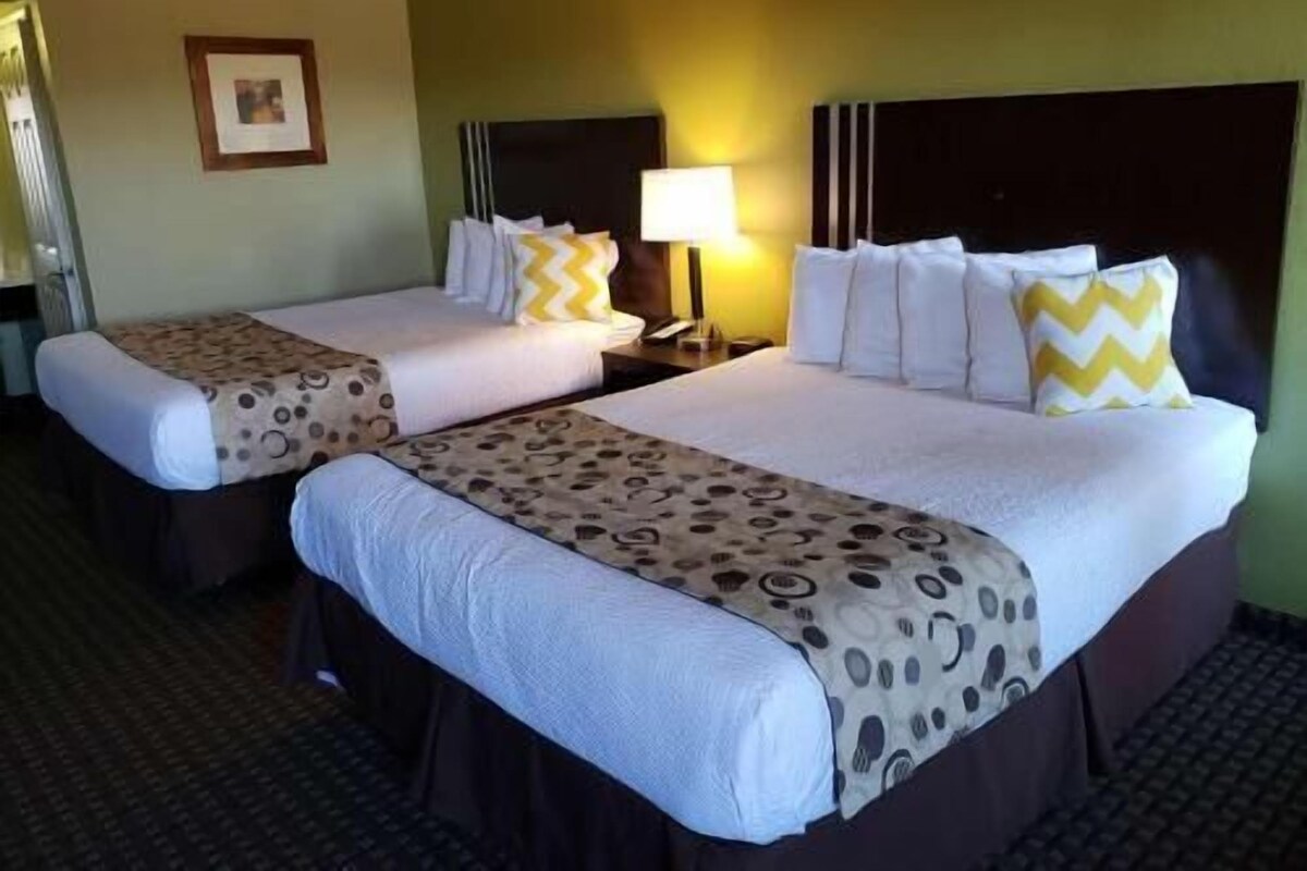 A hotel room with two beds, each with a patterned bedspread, a bedside lamp, and a framed picture on the wall.