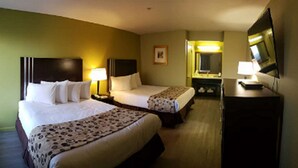 A hotel room with two beds, a desk, a television, and a mirror.