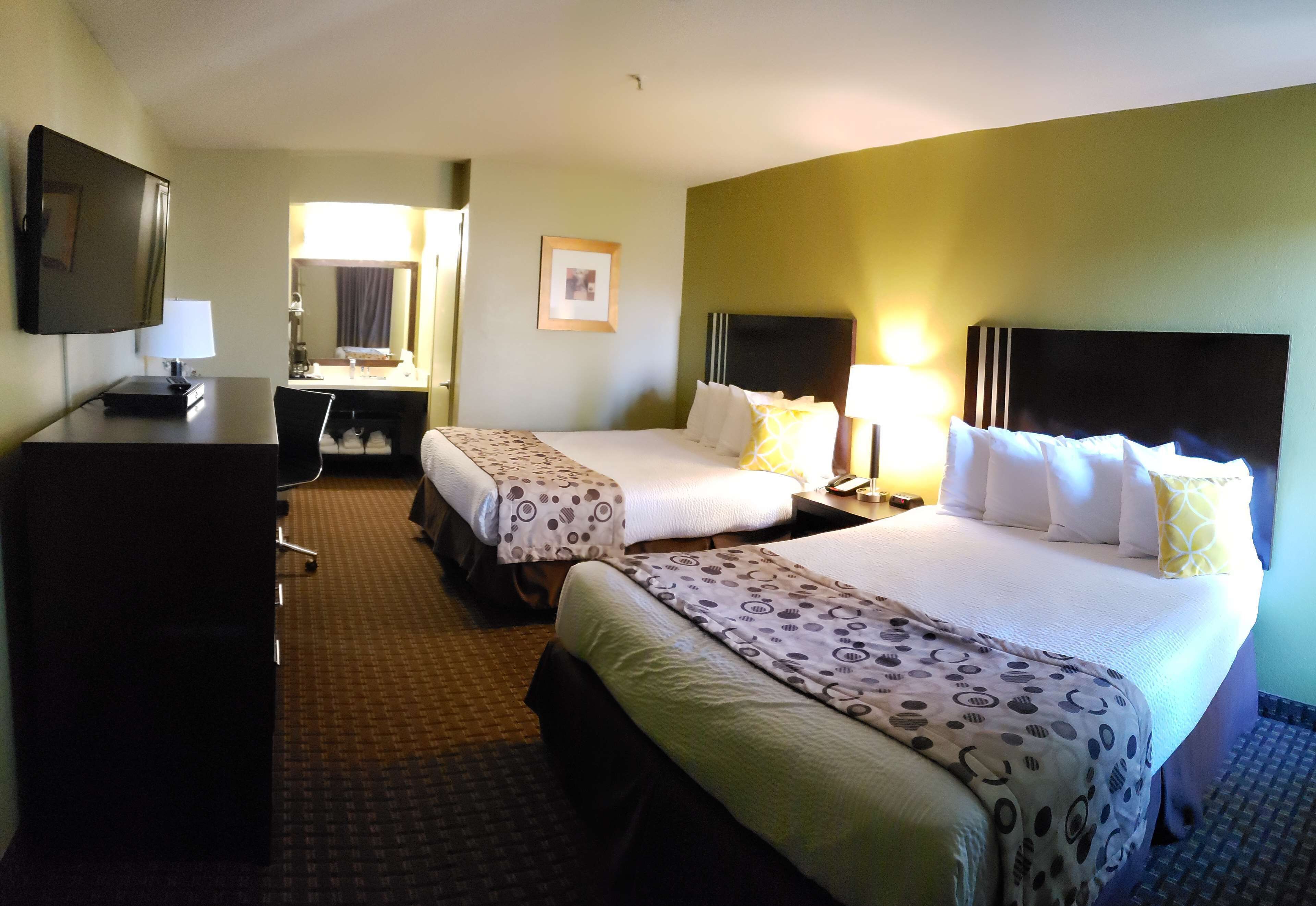 A hotel room with two beds, a desk, a television, and a mirror.