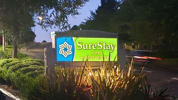 A SureStay Hotel sign with a recycling symbol, surrounded by plants and trees.