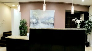 A reception desk with a painting of a bridge and trees, a potted plant, and a staircase to the left.