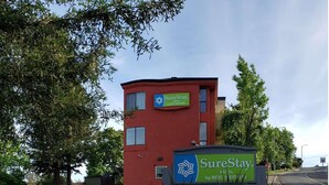 A red building with a SureStay hotel sign, surrounded by trees and a parking lot.