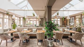 A spacious restaurant with high ceilings, large windows, and a variety of seating arrangements including tables and benches.