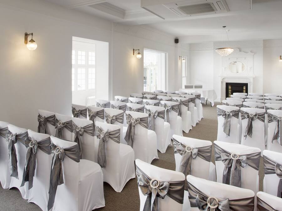 A conference room with rows of chairs covered in white fabric and gray sashes, a fireplace, and wall-mounted lighting.