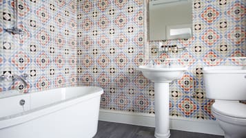 A bathroom with a geometric patterned tile wall, a white bathtub, a pedestal sink, and a toilet.