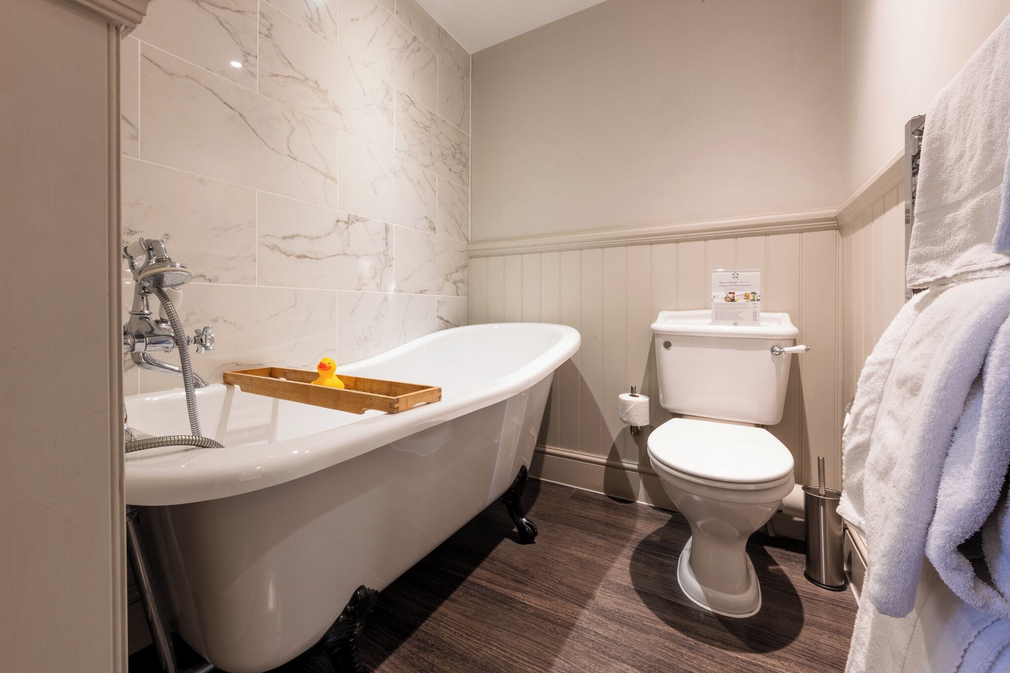 Une salle de bain avec une baignoire sur pieds, des toilettes et un plateau en bois avec une bougie.