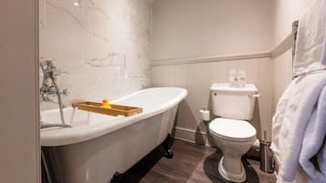 Une salle de bain avec une baignoire sur pieds, des toilettes et un plateau en bois avec une bougie.