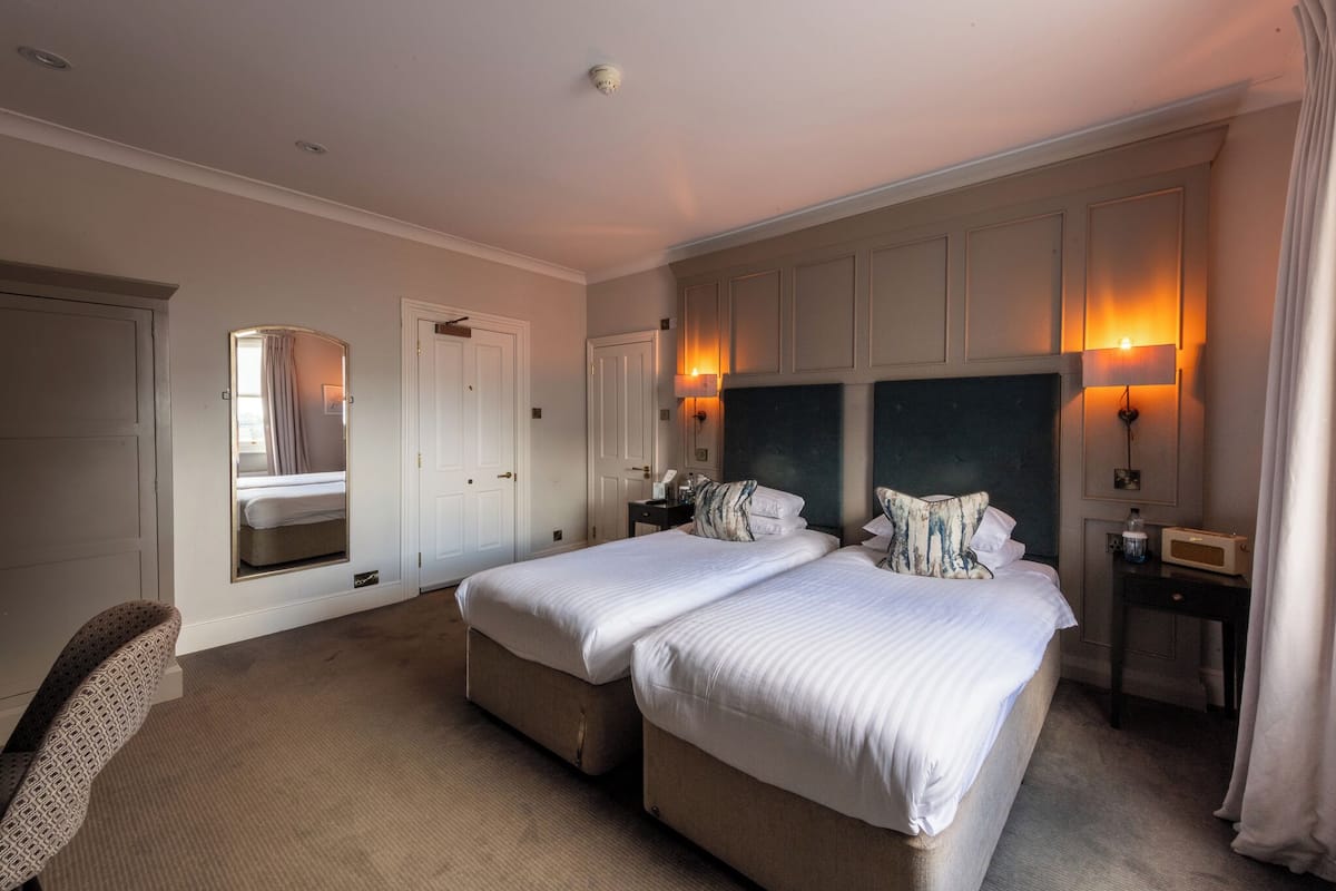 A hotel room with two beds, a sitting area, and a large mirror.