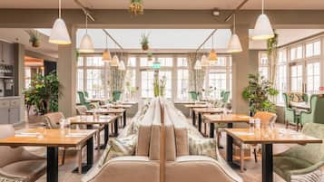 Un restaurant doté d’une longue table conviviale, de tables individuelles, de plantes suspendues et de luminaires suspendus.