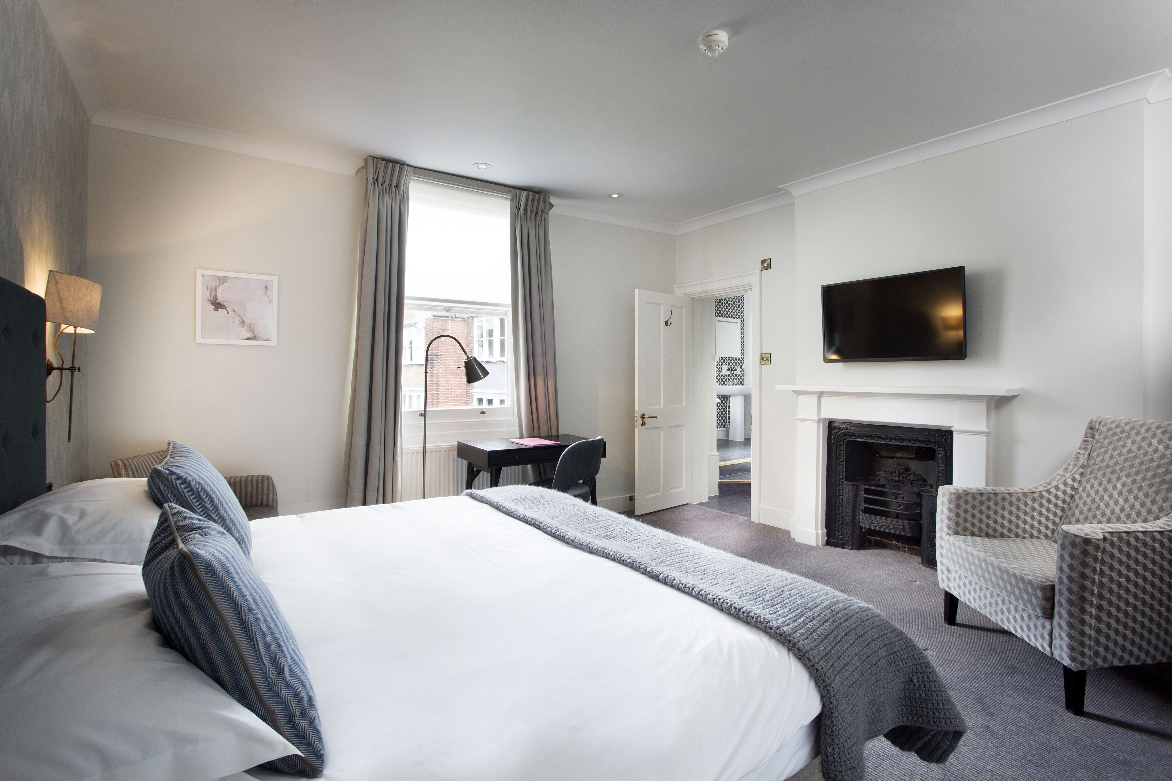 A hotel room with a large bed, a desk, a chair, a television, and a fireplace.