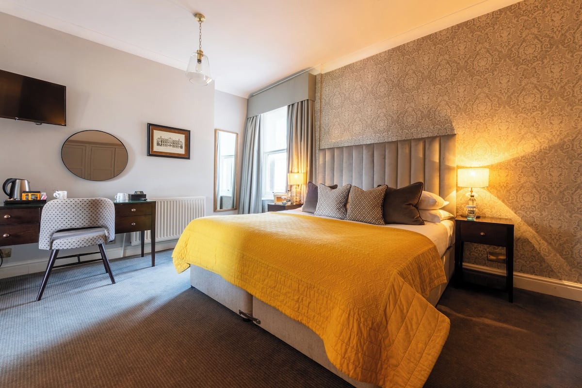 A hotel room with a large bed, a desk with a chair, a television, and a window with curtains.