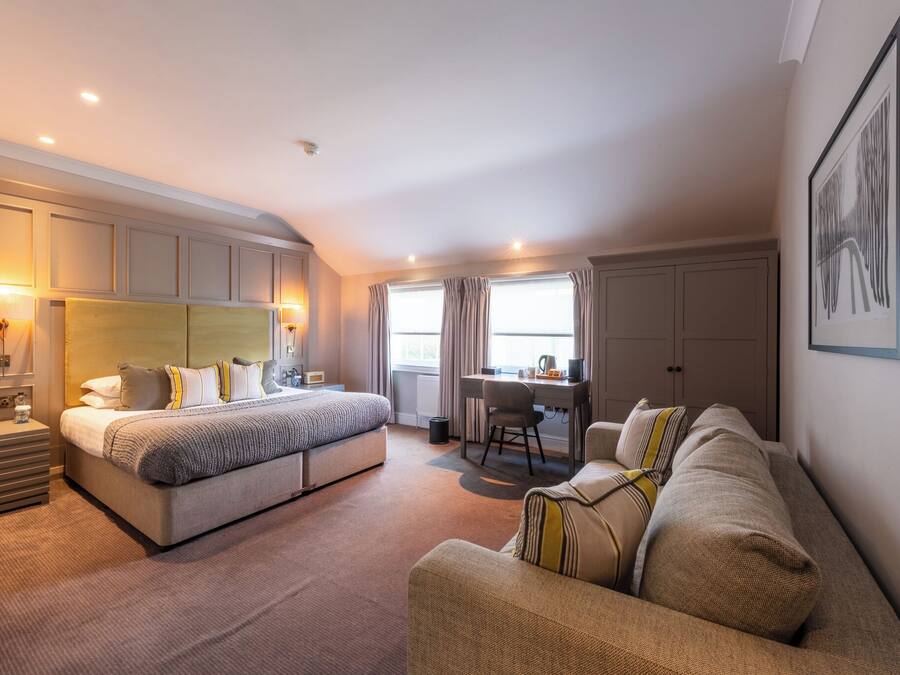 A modern hotel room with a large bed, a desk, and a sofa.