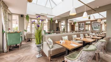 Un restaurante amplio con techos altos, ventanas grandes y diversas opciones de asientos, incluyendo cabinas y mesas.