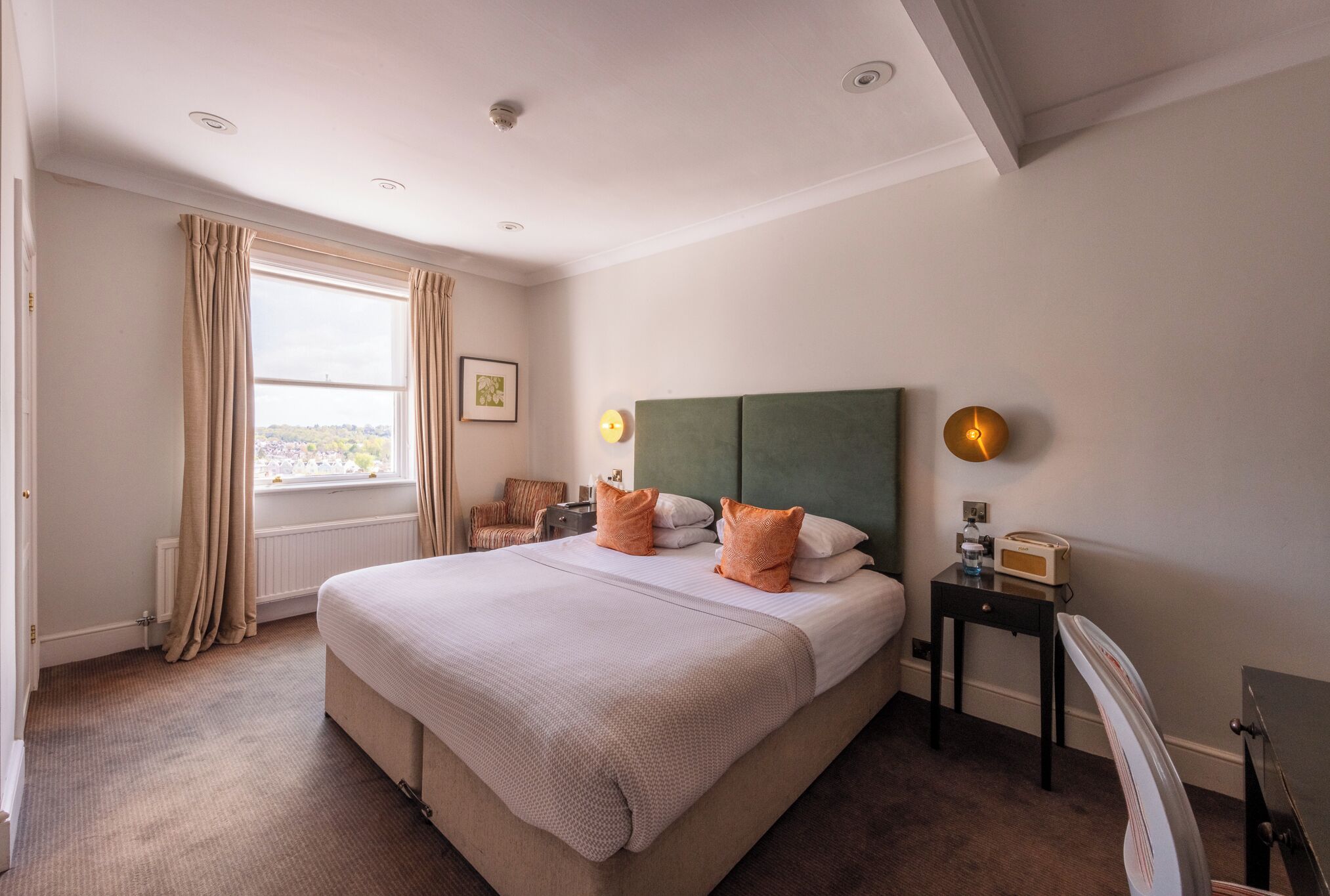 A hotel room with a large bed, a view of the city, a small table with a radio, and a green headboard.