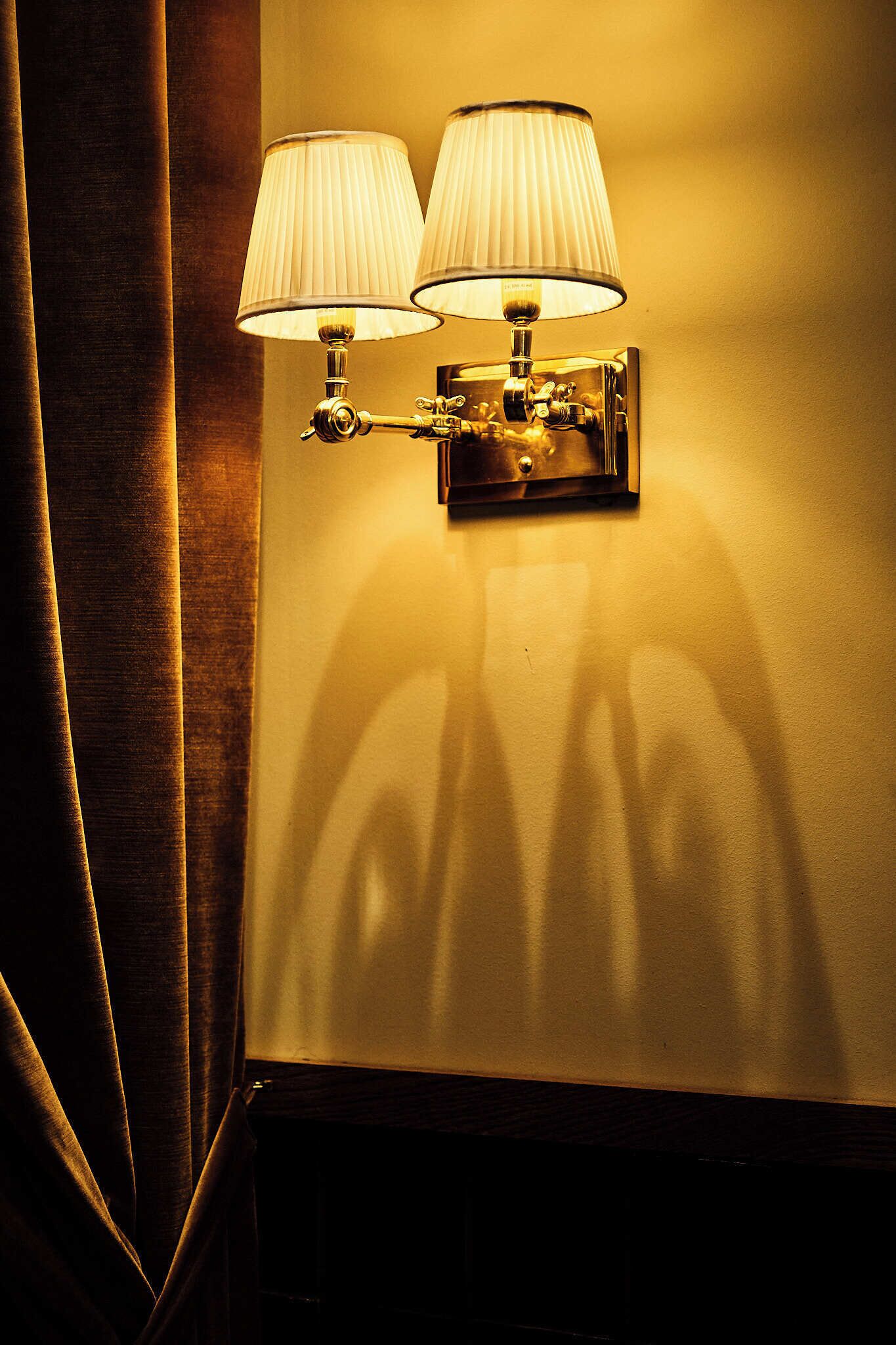 A wall-mounted lamp with two shades, casting shadows on a wall.