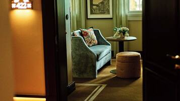 A hallway leading to a room with a sofa, a round table with flowers, and framed pictures on the wall.