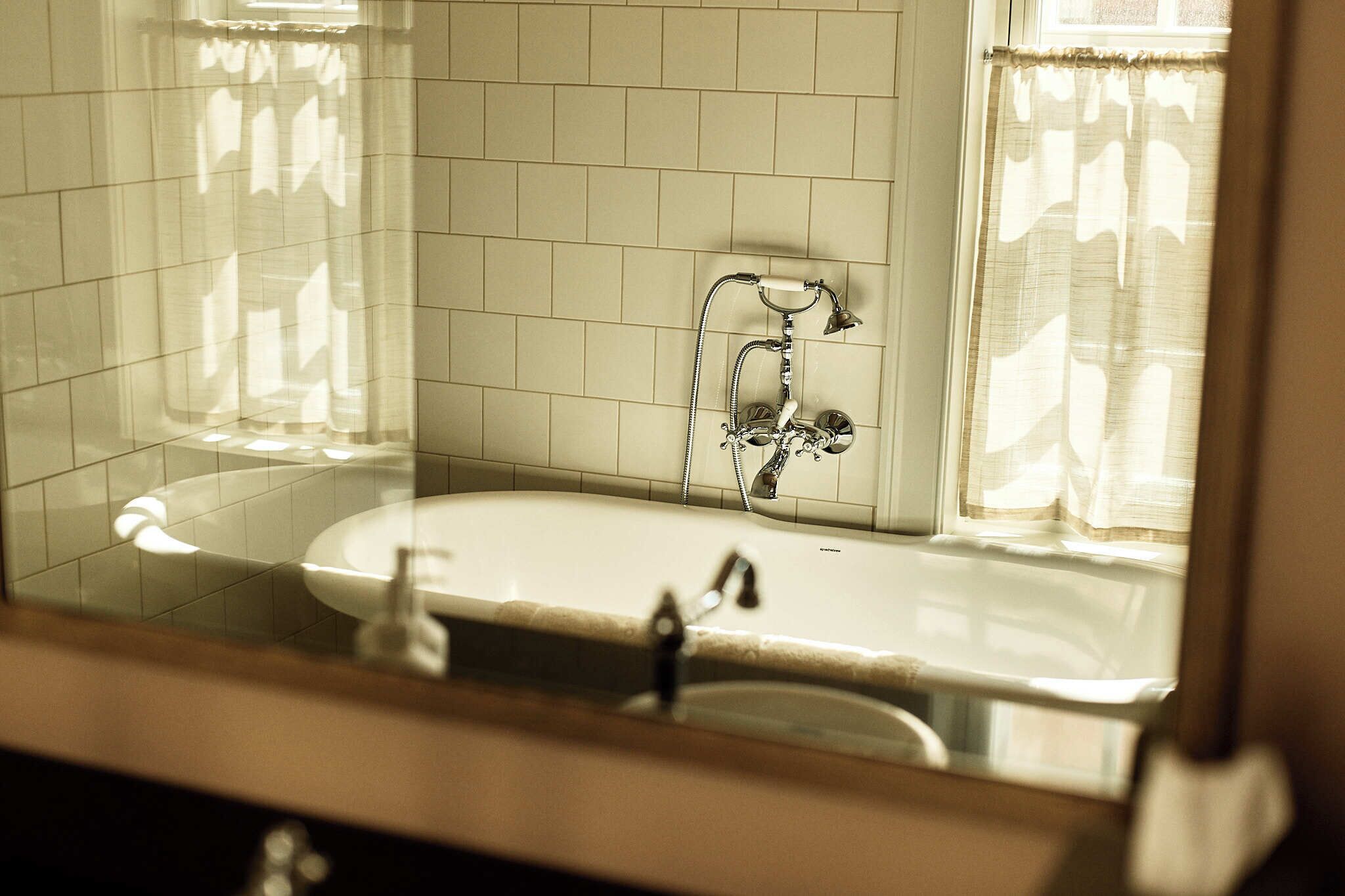 A bathroom with a white tiled wall, a bathtub, and a shower with a chrome faucet.