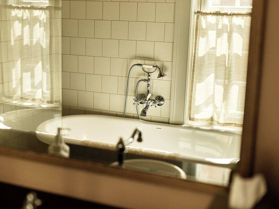 A bathroom with a white tiled wall, a bathtub, and a shower with a chrome faucet.