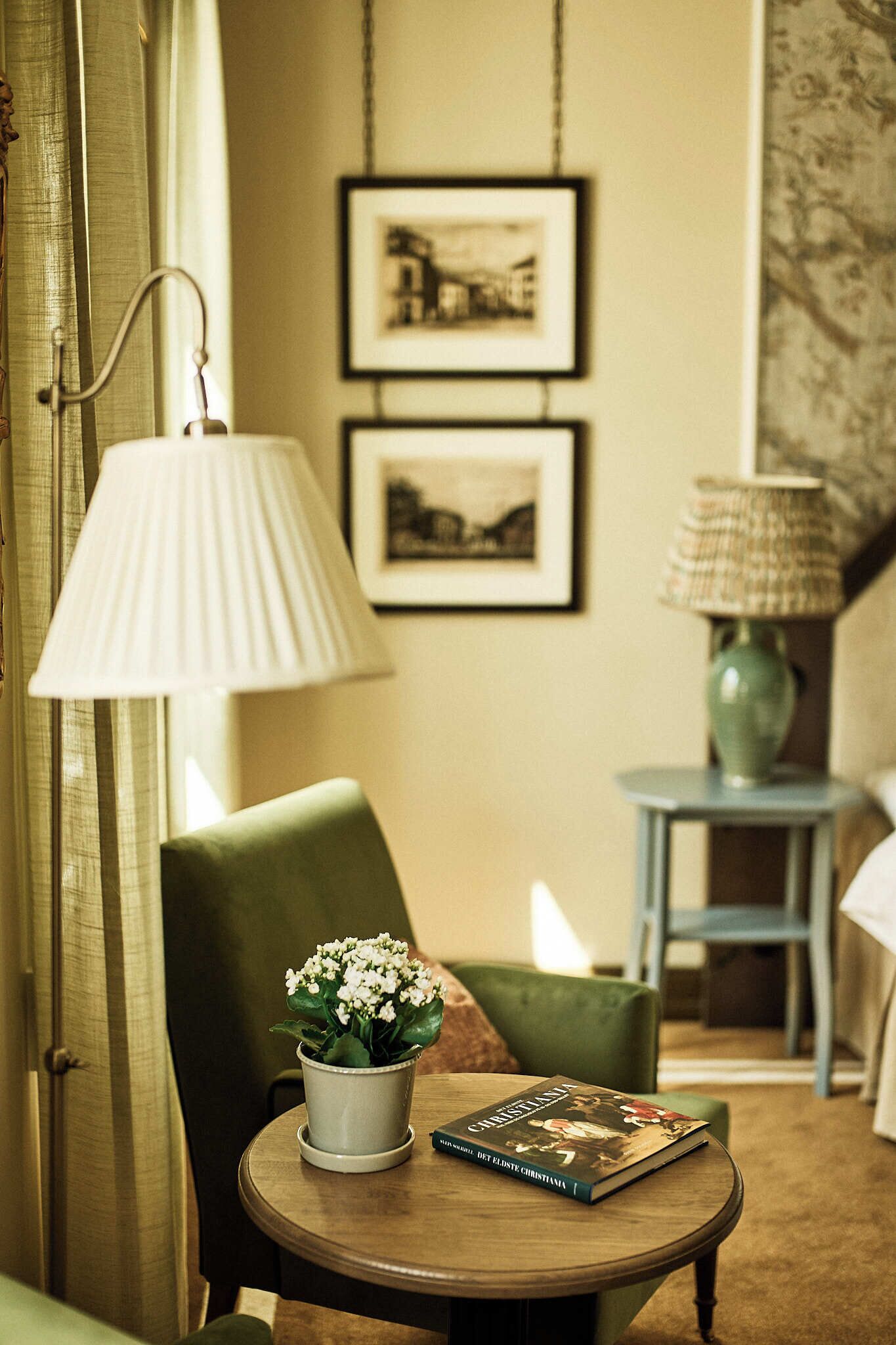 Ein Zimmer mit einem runden Holztisch, einem Stuhl, einer Lampe, einer Vase mit Blumen und zwei gerahmten Bildern an der Wand.