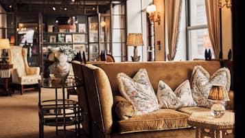 Una habitación acogedora con un sofá marrón, cojines decorativos, una mesita redonda con una lámpara y una silla.
