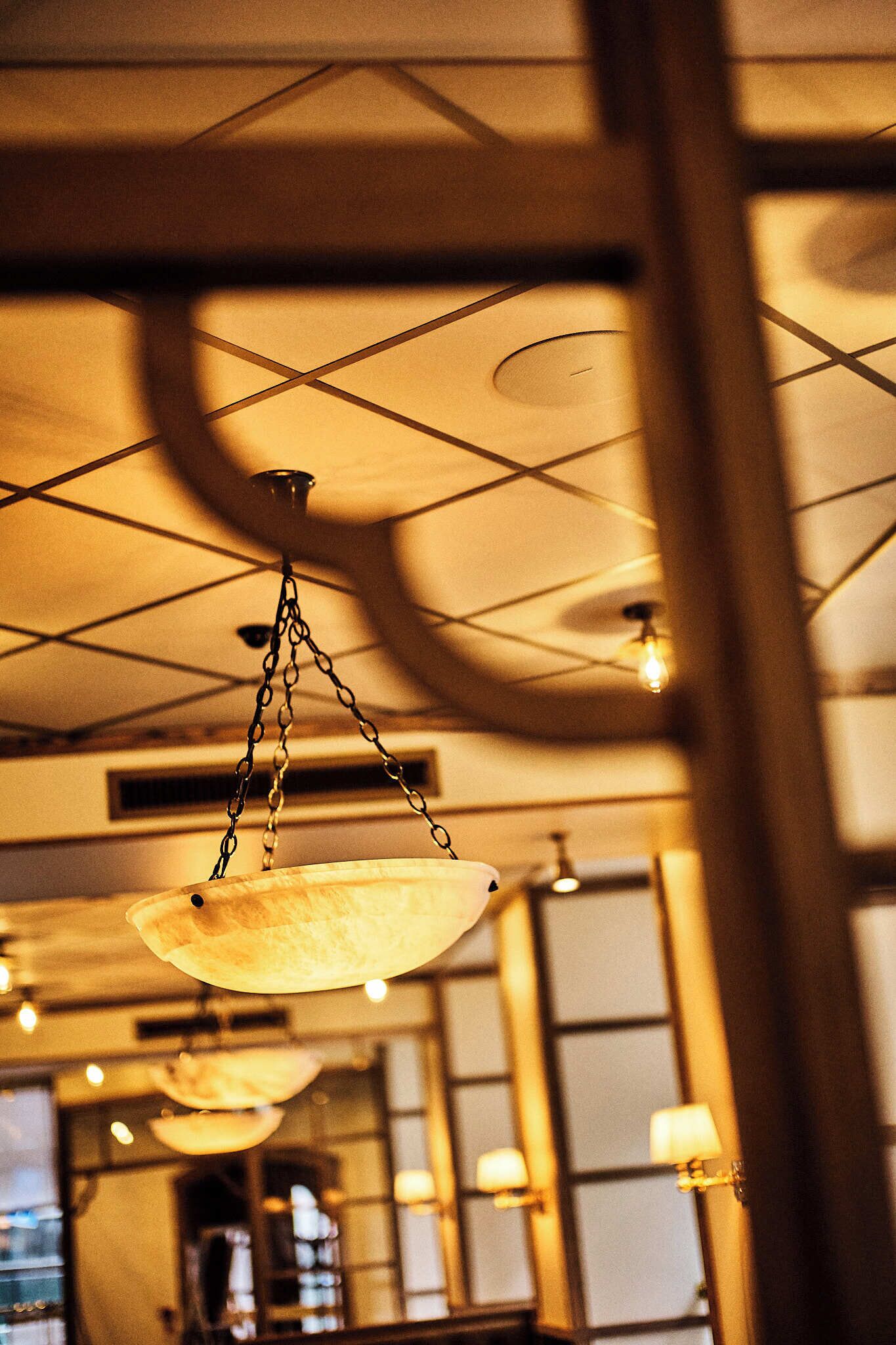 A hanging light fixture with a chain and a bulb, a ceiling with a grid pattern, and a wall with a window and a lamp.