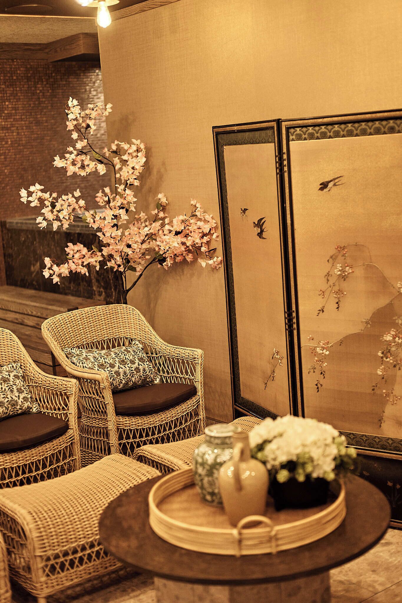 A room with wicker furniture, a vase with flowers, and a framed artwork with birds.