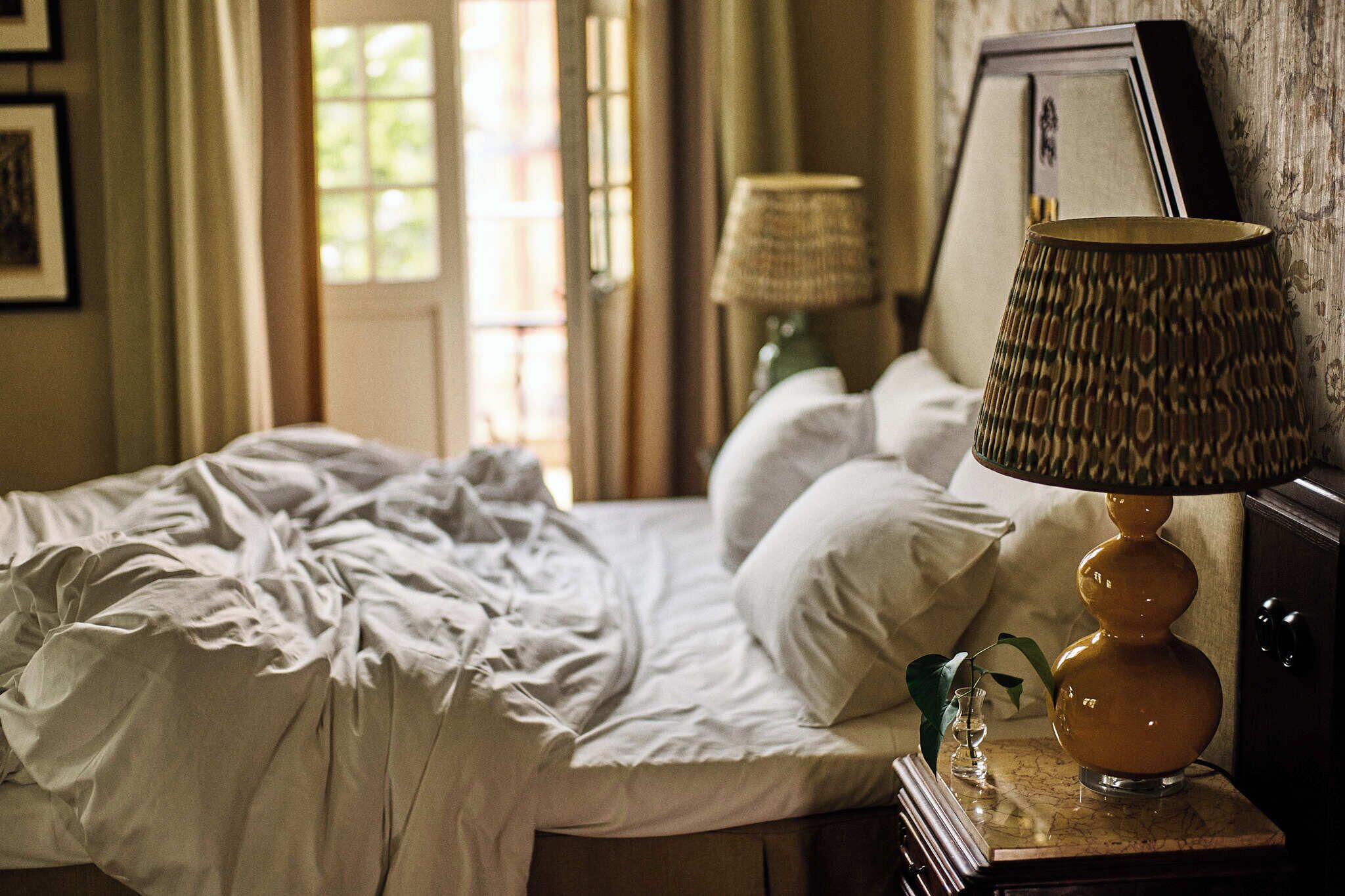 A bedroom with a bed, a lamp, a small vase, and a picture frame on a nightstand.