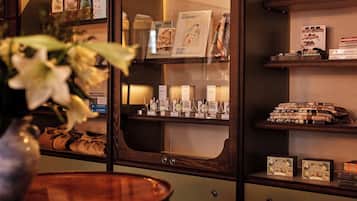 A hotel room with a minibar, a vase with flowers, and a shelf with books and bottles.