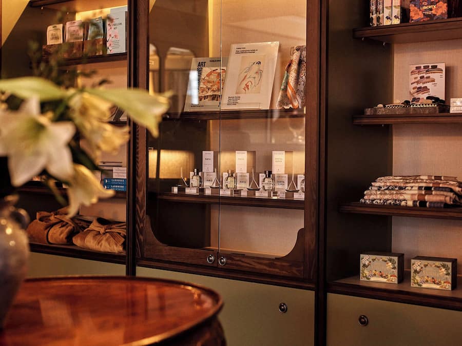 A hotel room with a minibar, a vase with flowers, and a shelf with books and bottles.