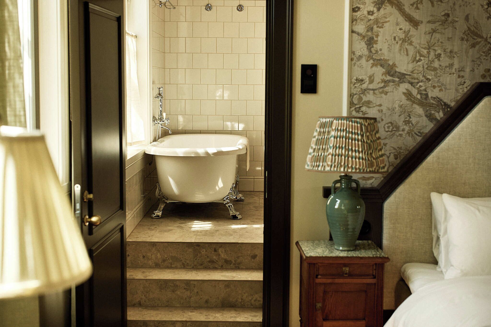 Una habitación con una bañera, una lámpara y una cama.