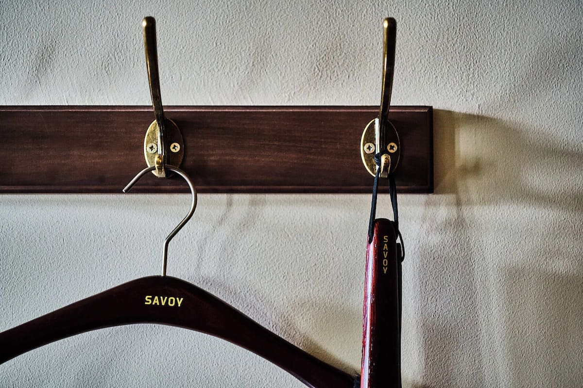 Un porte-manteau en bois doté de deux crochets, d’un cintre en métal et d’une marque bien visible, « SAVOY ».