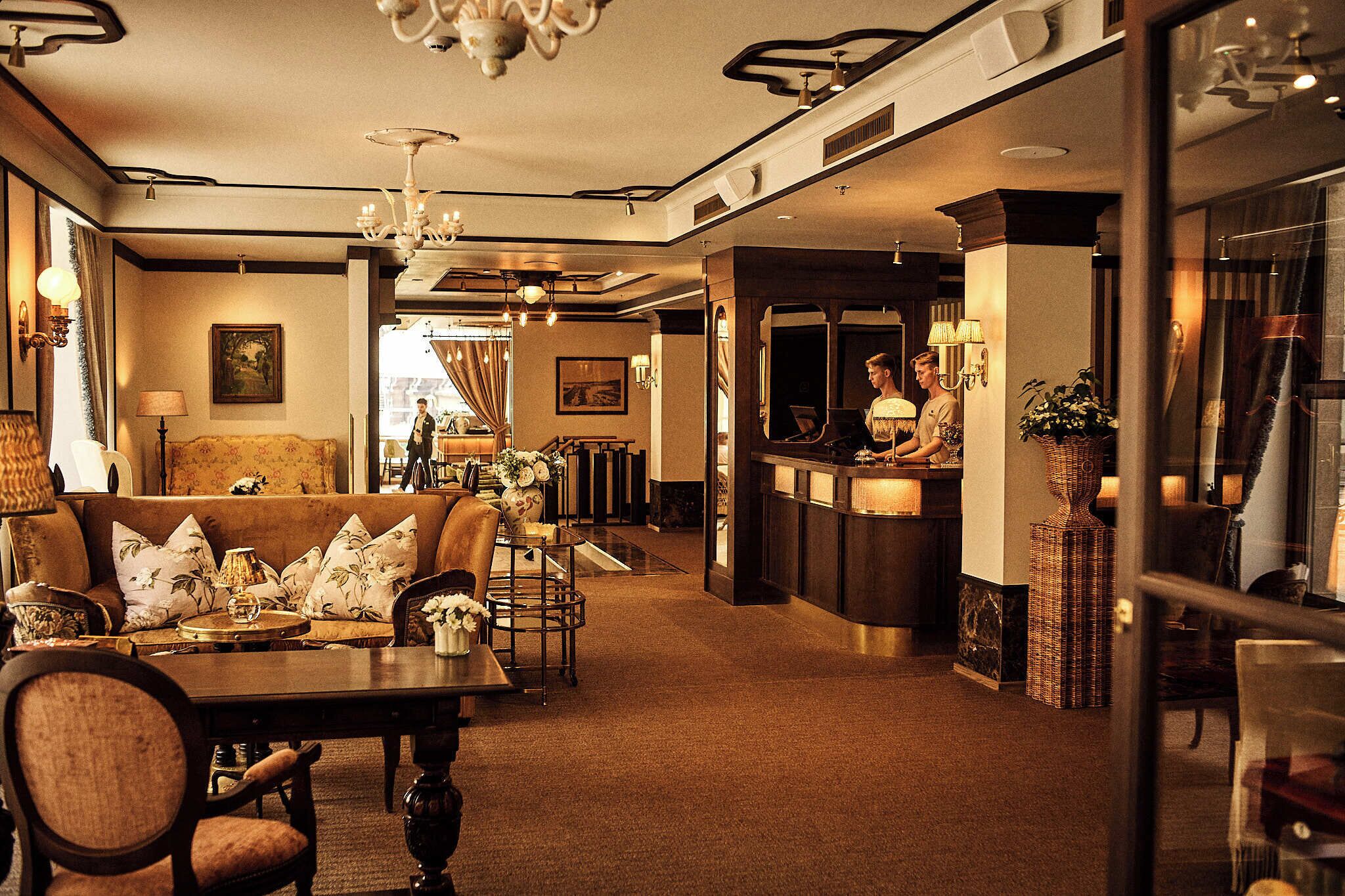 Un hall d’hôtel comprenant un comptoir d’accueil, un espace salon et un lustre.