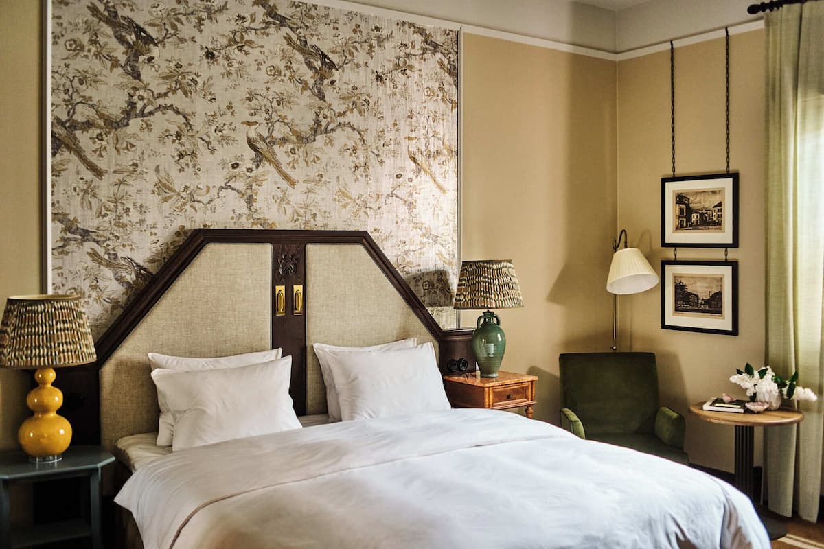 Une chambre d’hôtel avec un grand lit, deux tables de chevet, une chaise, une petite table avec une lampe et un mur orné de tableaux.