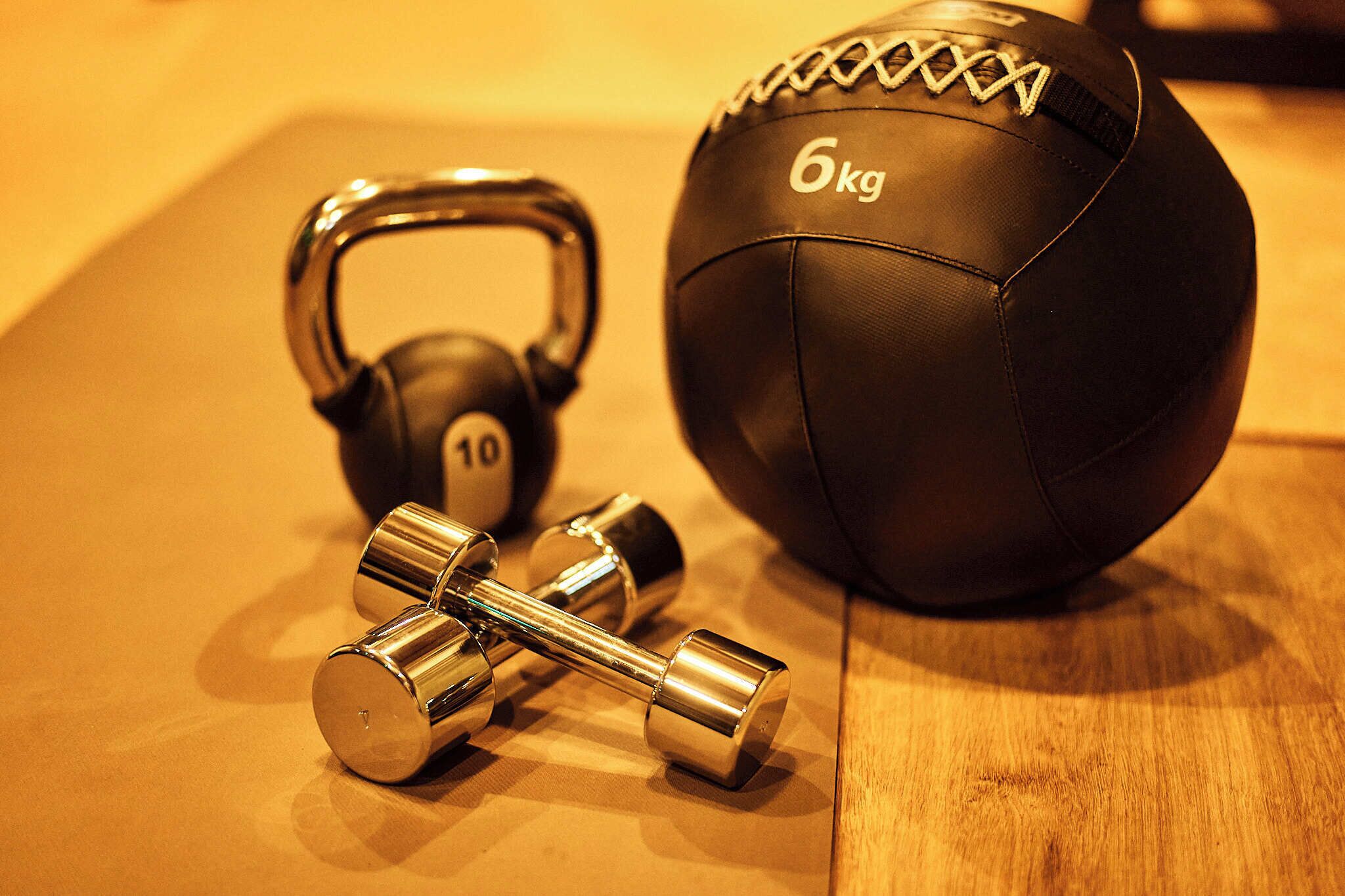 A pair of dumbbells and a sports ball on a wooden surface.