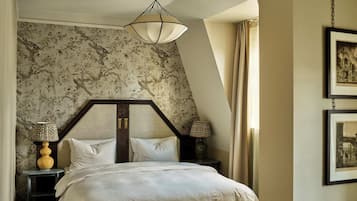 Un dormitorio con cama, mesita de noche, lámpara, un cuadro en la pared y una ventana con cortinas.