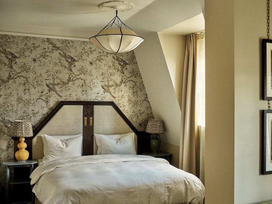 Un dormitorio con cama, mesita de noche, lámpara, un cuadro en la pared y una ventana con cortinas.