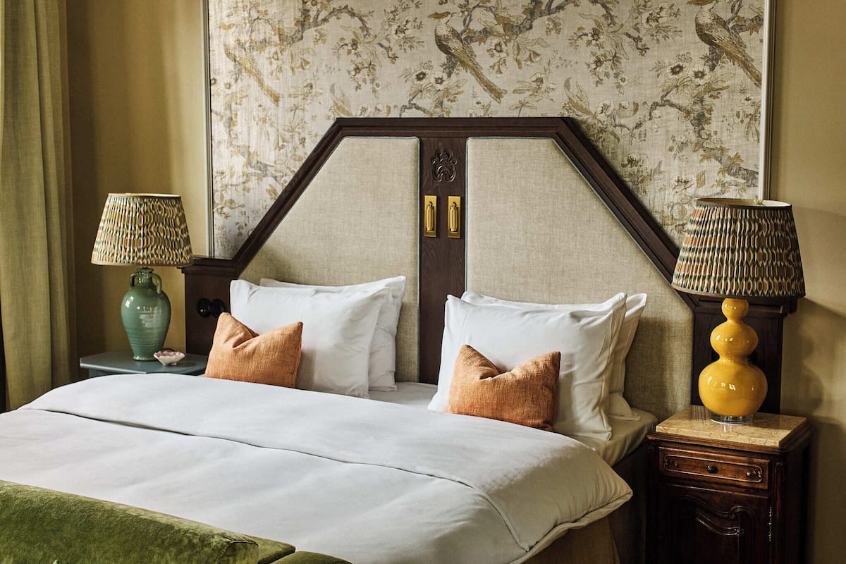 Une chambre d’hôtel avec un lit, deux tables de chevet, des lampes et un papier peint à motifs floraux.
