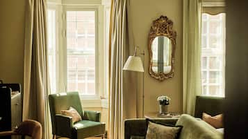 Una habitación con un sillón verde, una lámpara de pie, un espejo y una ventana con cortinas.
