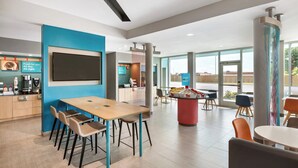 A modern dining area with a long table, chairs, a coffee station, and a large window providing a view. - avid Hotel Ocala Downtown by IHG (Ocala)