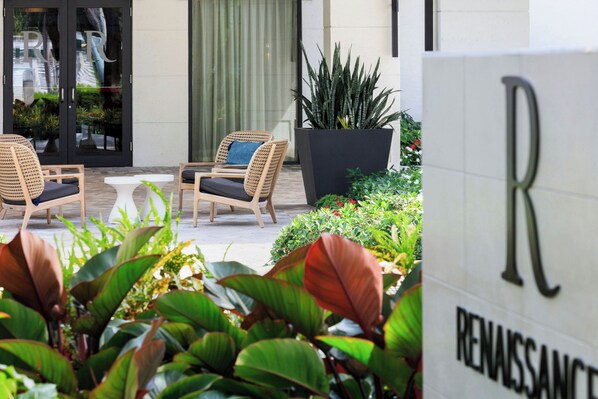 L’entrée d’un hôtel, avec une enseigne indiquant « RENAISSANCE », des chaises en osier, une plante en pot et une petite table.