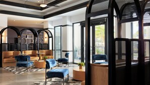 Eine moderne Lobby mit einer Sitzecke, ausgestattet mit Sofas und Sesseln, großen Fenstern und einem gemusterten Teppich.