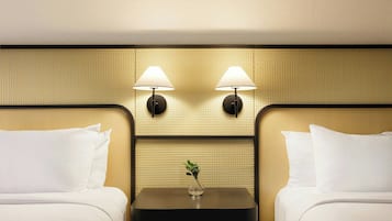 A hotel room with two beds, a small table with a vase, and two wall-mounted lamps.