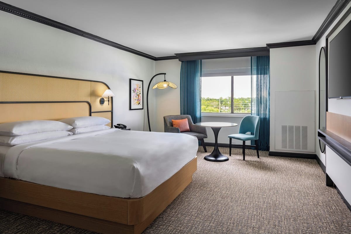 A hotel room with a large bed, a desk, a chair, a lamp, a TV, and a window with curtains.