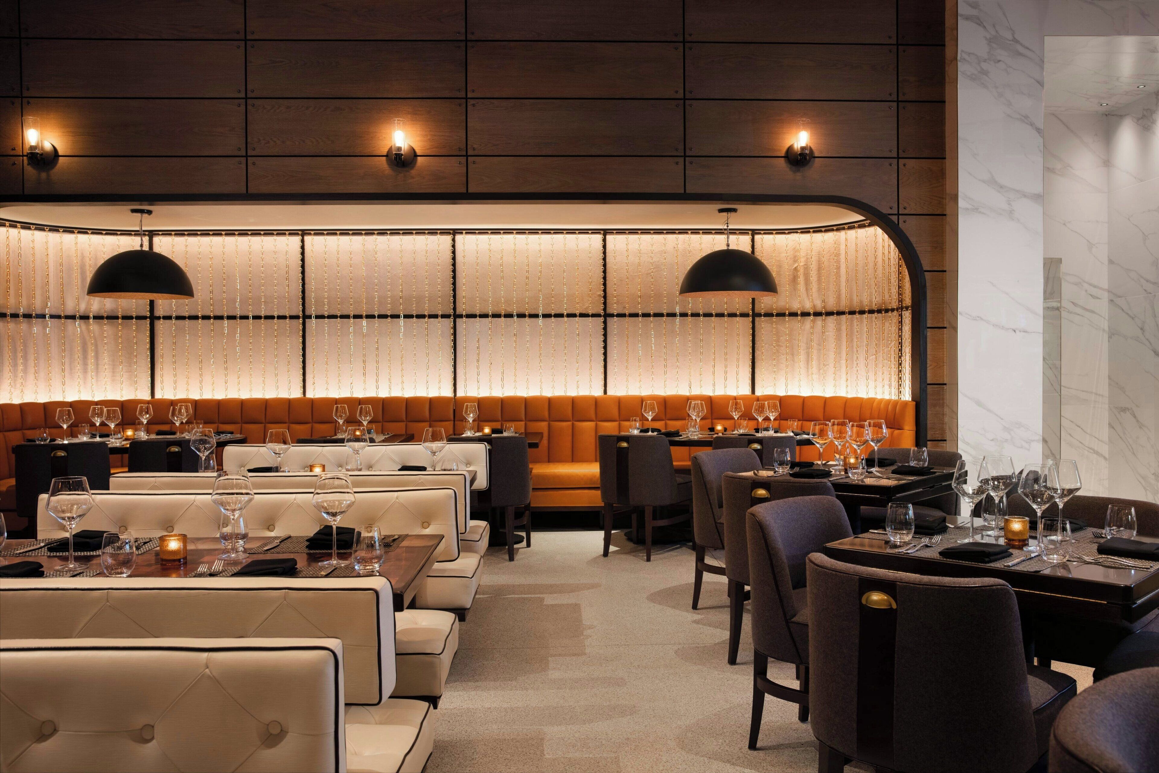 A restaurant with a long, illuminated wall, cushioned seating, and pendant lighting.