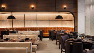 A restaurant with a long, illuminated wall, cushioned seating, and pendant lighting.