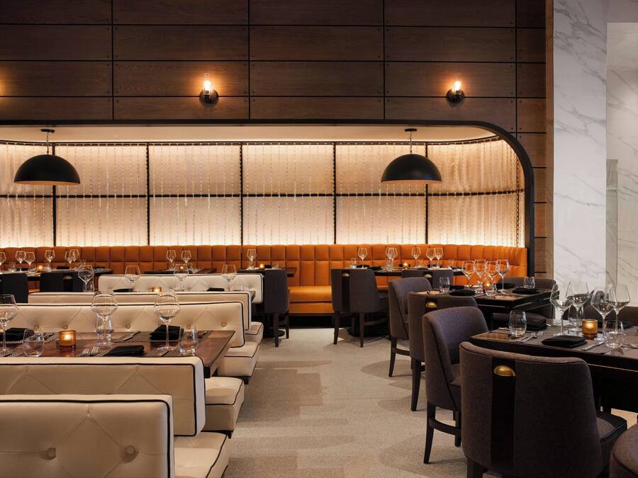 A restaurant with a long, illuminated wall, cushioned seating, and pendant lighting.