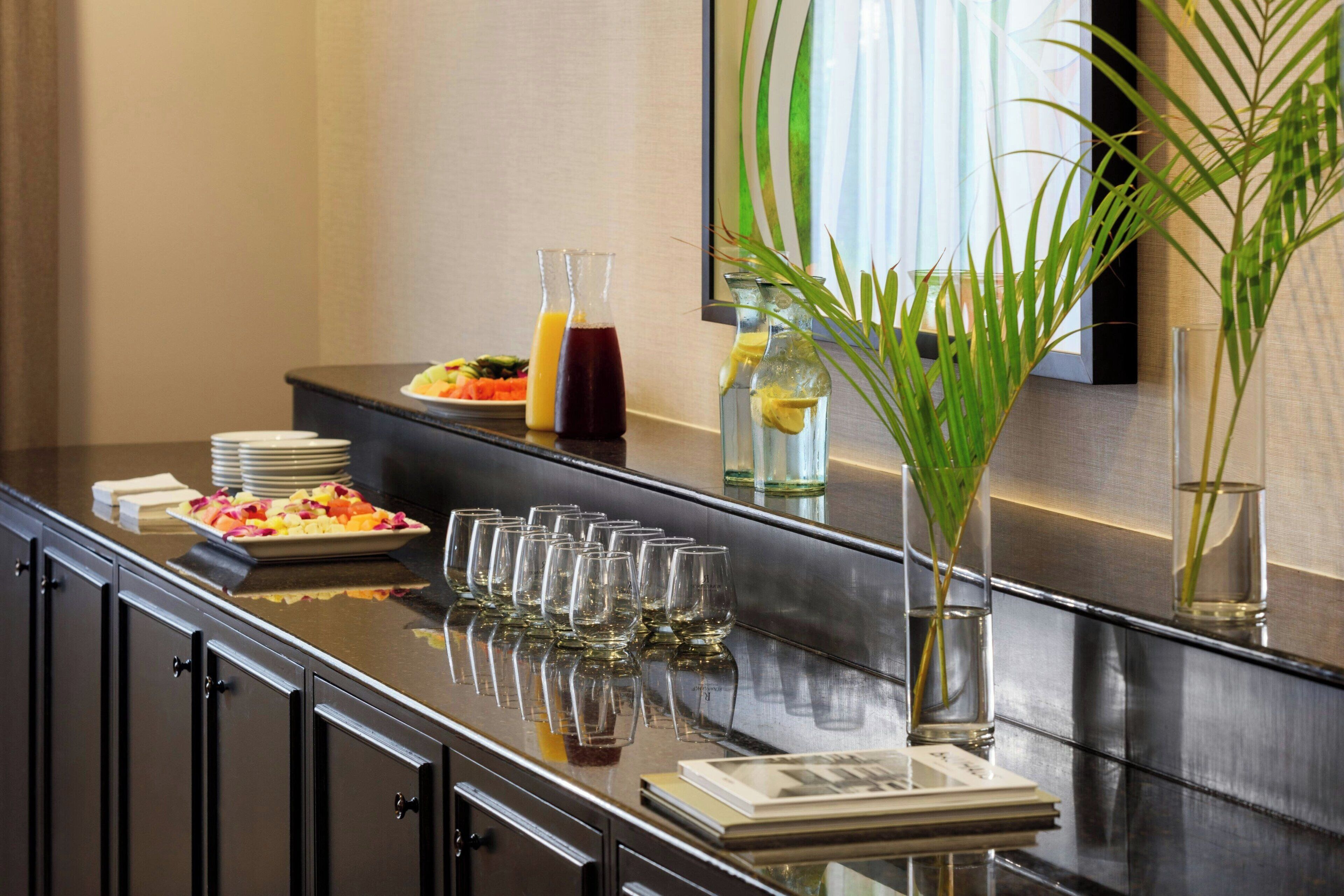 A breakfast bar with plates of food, glasses, and a vase with a plant.