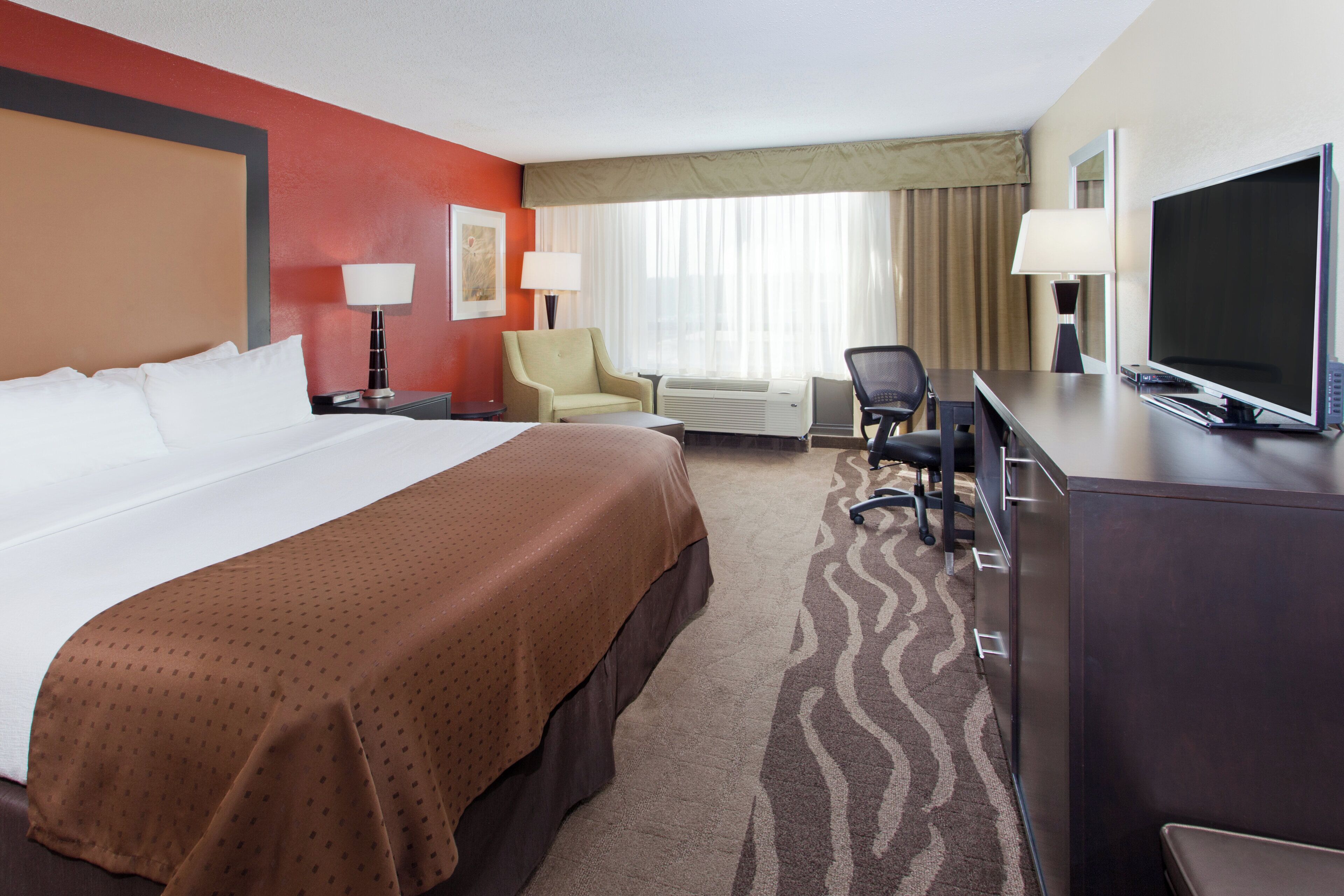 Quarto de hotel com cama grande, escrivaninha com televisão, cadeira e abajur.