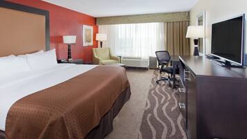 Quarto de hotel com cama grande, escrivaninha com televisão, cadeira e abajur.