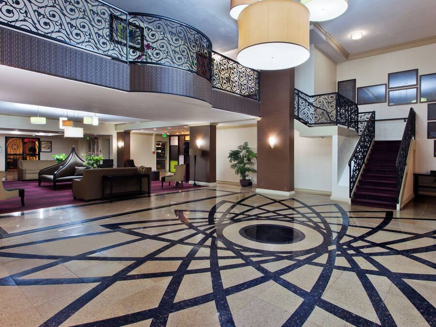 A spacious lobby with a geometric patterned floor, a curved balcony with ornate railings, and a staircase with a black metal railing.